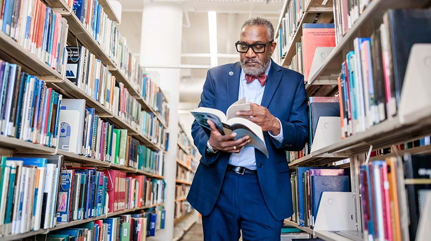 Dr. Alfred Tatum stands in the library reading a book.